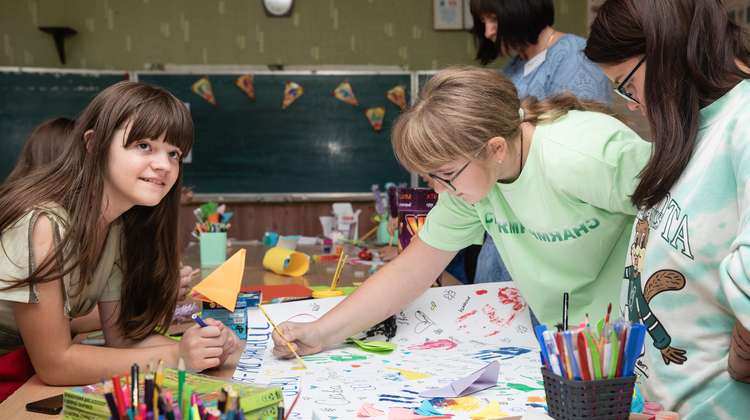 Kinder in einem Klassenzimmer stehen um einen Tisch und malen