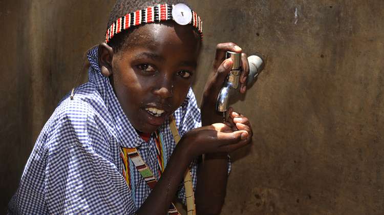 Ein kenianisches Kind benutzt einen Wasserhahn.