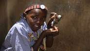 Ein kenianisches Kind benutzt einen Wasserhahn.