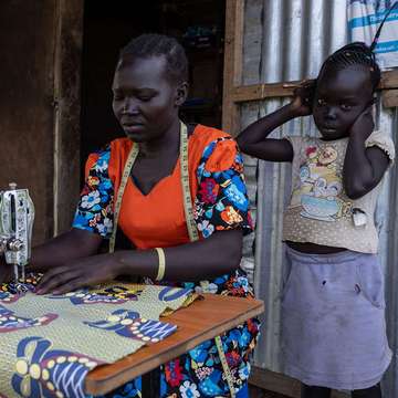 Frau in Uganda arbeitet an einer Nähmaschine, neben ihr ein Kind