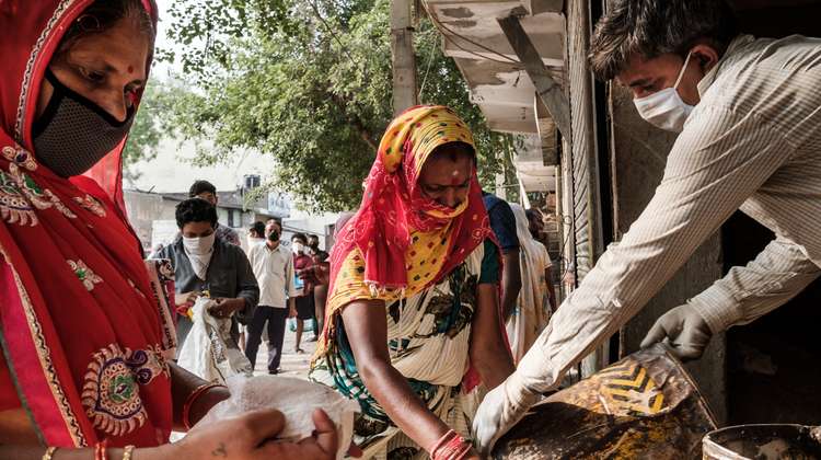 Frauen mit Maske verteilen Lebensmittel, Indien.