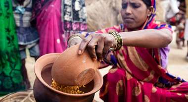 Eine Frau im Sari mit einem Ton-Gefäß in der Hand, das gefüllt ist mit Essen.