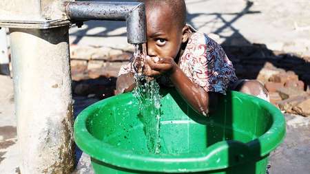A boy drinks water from the faucet