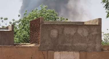 Kind steht vor einem Haus im Sudan nach Ausbruch des Krieges, es steigt Rauch auf.