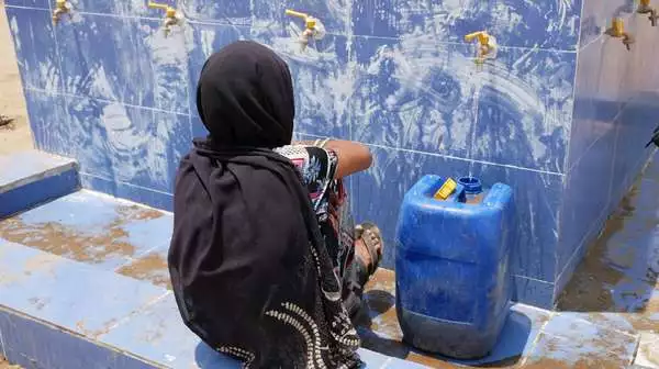 Eine Frau wartet an einer Wasserstelle darauf, dass ihr Kanister mit Trinkwasser voll wird.