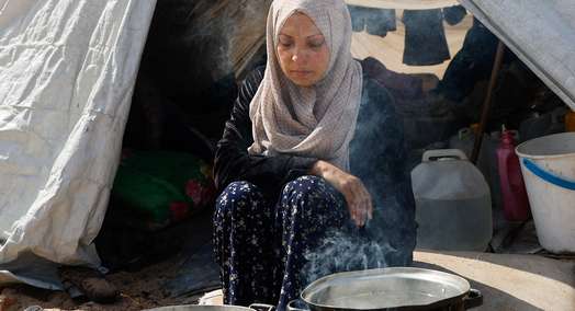 Eine Frau sitzt beim Kochen vor zwei Töpfen draußen vor einem Zelt