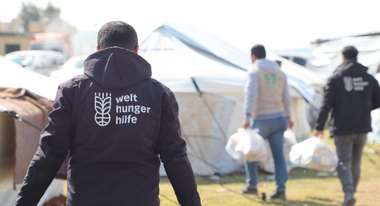 Verteilung warmer Mahlzeiten in einem Flüchtlingscamp in Syrien. Im Vordergrund ein Helfer mit Welthungerhilfe-Logo auf der Rückseite seiner Jacke.