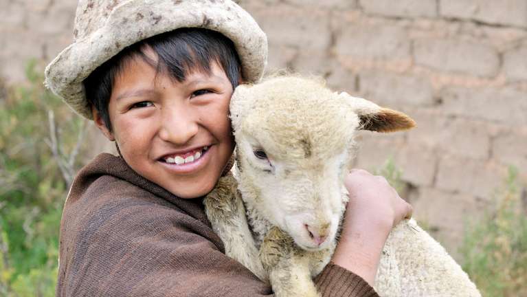 Ein bolivianischer Junge hält ein ein Lamm im Arm.
