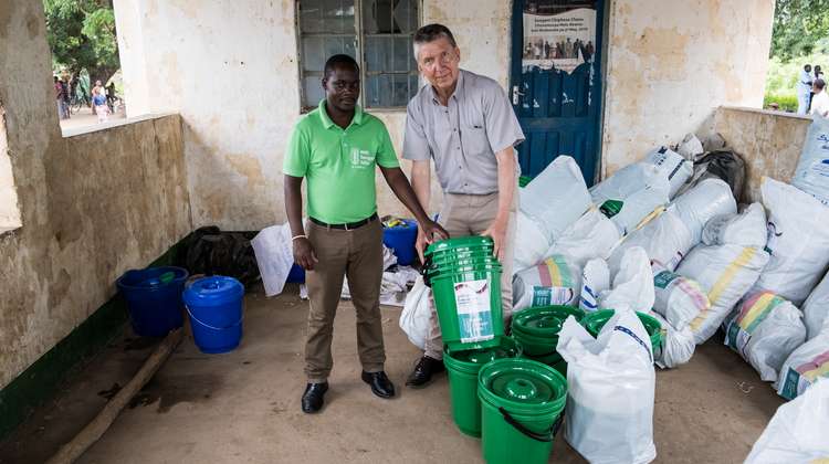 Zwei Männer, einer davon trägt ein grünes Welthungerhilfe-T-Shitrt, stehen vor großen Säcken voller Hilfsgüter.