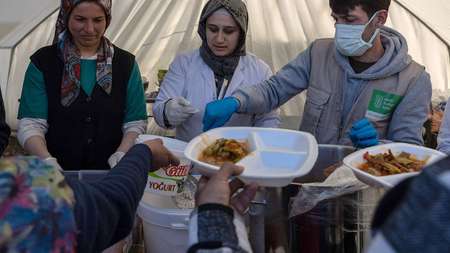 Zwei Frauen und ein Mann stehen in einem Zelt und verteilen Mahlzeiten.
