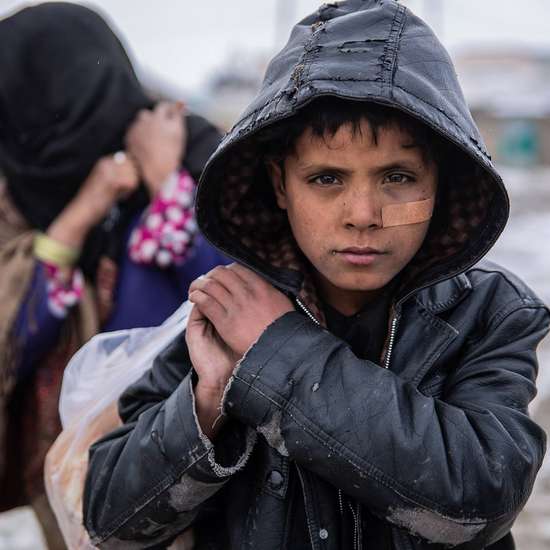Winterhilfe in Afghanistan - Jetzt spenden. Bild: Ein Junge mit Kapuze trägt eine Tüte und blickt in die Kamera. Im Hintergrund sieht man Schnee.