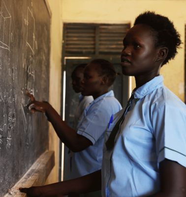 Bild aus einem Projekt im Südsudan mit Schulspeisungen, ein Mädchen steht an einer Schultafel.