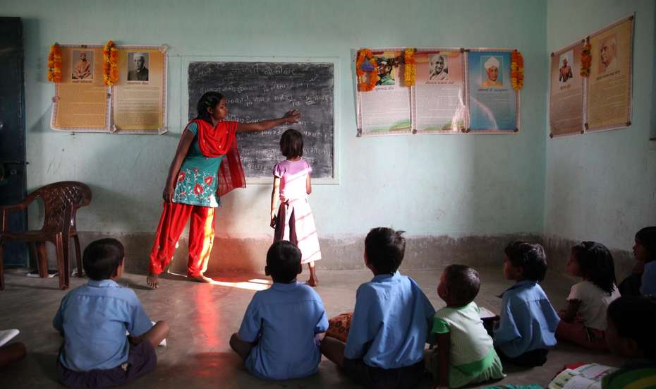 Kinder sitzen in einem Klassenraum auf dem Boden und schauen gespannt auf die Tafel
