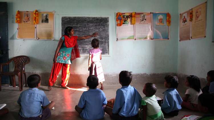 Kinder sitzen in einem Klassenraum auf dem Boden und schauen gespannt auf die Tafel