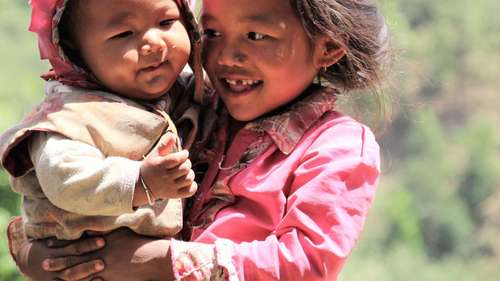 Jetzt Spenden an Weihnachten. Bildbeschreibung: Ein lachendes Mädchen in Nepal mit einem Baby auf dem Arm.