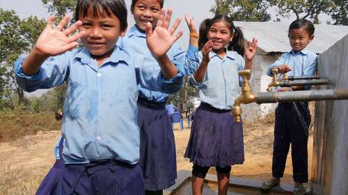 Hilfe für Nepal - Bild: WASH-Projekt in Nepal: Kinder stehen winkend vor Wasserhähnen.