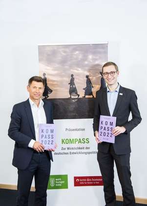 Zwei Männer halten den Bericht "Kompass 2022" und lächeln in die Kamera.