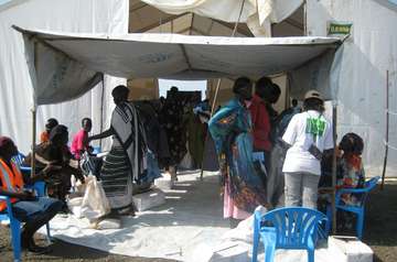 Refugees are waiting in front of a tent for food.