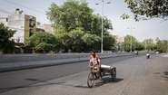Ein Rikscha Fahrer auf einer fast leeren Straße in Delhi, Indien.