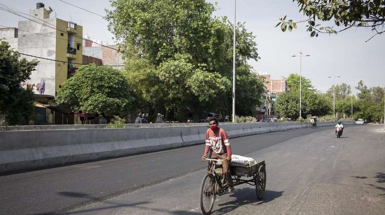 Ein Rikscha Fahrer auf einer fast leeren Straße in Delhi, Indien.