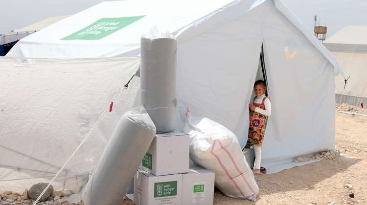 Ein weißes Zelt mit Welthungerhilfe-Logo, ein Mädchen steht im Eingang und schaut in die Kamera.