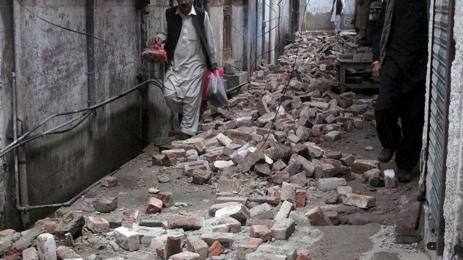 Ein Mann läuft mit seinen Habseligkeiten durch die Trümmer seines Hauses in Pakistan.