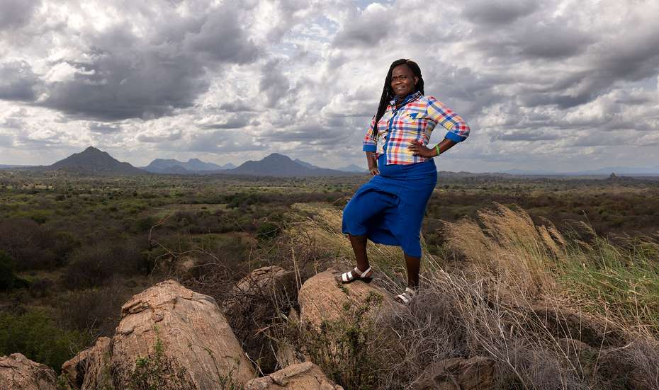 Josephine Mbuvi steht auf einem Felsen in der Landschaft und schaut selbstbewusst Richtung Kamera.