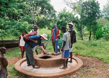 Bewohner stehen um einen Schachtbrunnen für Wasser verteilt.