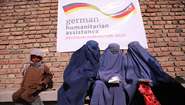 Drei Frauen mit blauen Burkas und ein Junge warten bei einer Lebensmittelverteilung in Kabul, Afghanistan. 