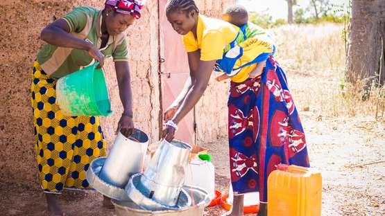 Frauen säubern den Futtertank der Hühneraufzucht in Kongoussi, Burkina Faso.