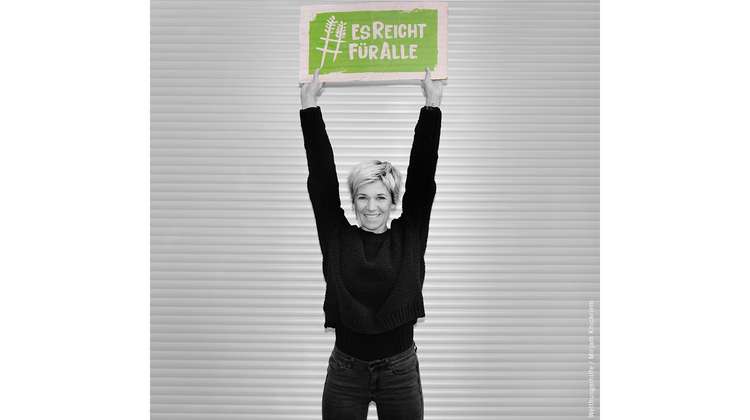 Schauspielerin Kerstin Landsmann hält ein Schild mit dem Welthungerhilfe-Hashtag #EsReichtFürAlle über den Kopf.