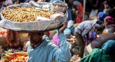 Ein Mann trägt einen großen Teller mit Essen auf dem Kopf bei einem Markt im indischen Jamshedpur. 