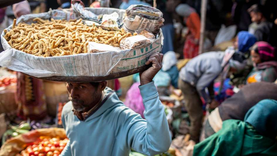 Ein Mann trägt einen großen Teller mit Essen auf dem Kopf bei einem Markt im indischen Jamshedpur. 