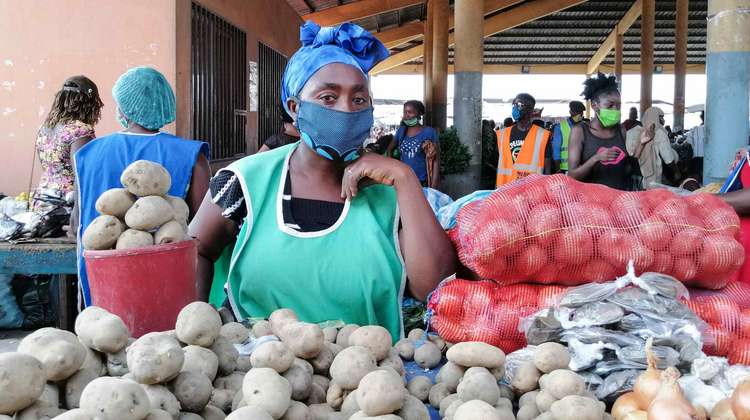 Eine Frau mit Maske hinter ihrem Marktstand, Angola.