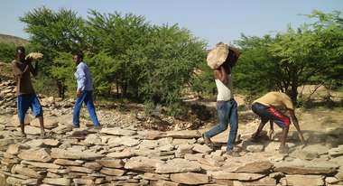 Männer tragen Steine und bauen einen Damm