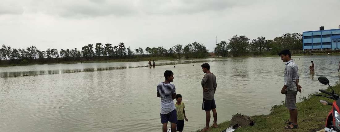 Menschen stehen vor überfluteten Feldern nach Zyklon Amphan, Indien.
