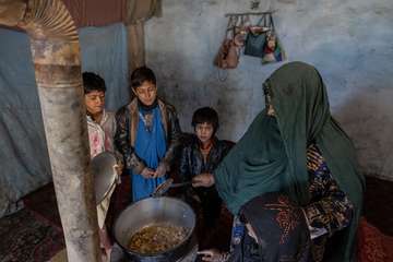 Mutter in Afghanistan sitzt mit ihren Kindern um einen Topf mit Mittagessen.