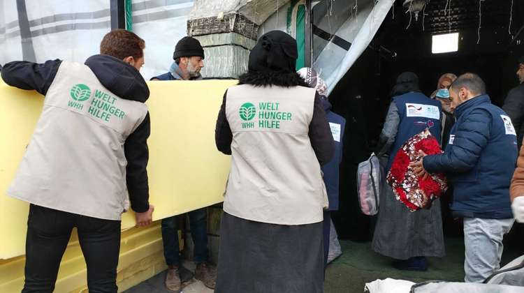 Mitarbeiter:innen der Welthungerhilfe tragen Schaumstoffmatratzen in eine Notunterkunft
