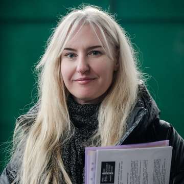Eine Frau mit Dokumenten in der Hand. Sie lächelt in die Kamera.