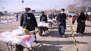 Lebensmittelverteilung in Kabul, Afghanistan: Männer schieben Schubkarren beladen mit Säcken voller Nahrungsmitteln.