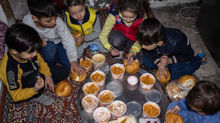 Sechs Kinder sitzen im Kreis um eine Platte voller frischer Mahlzeiten in Transportboxen und bedienen sich.