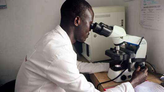Laborassistent Lochap John Robert aus Uganda schaut durch ein Mikroskop.