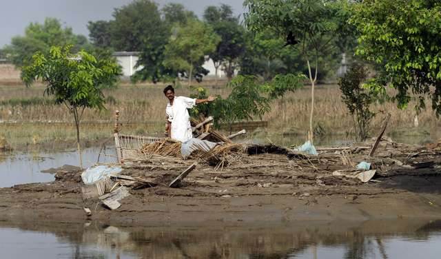 Ein Mann steht auf einem von Wasser umgebenen Stück Land und zeigt auf zerstörte Haushaltsgegenstände.