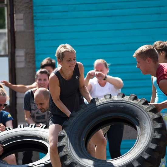 Menschen in Sportklamotten rollen große Reifen.
