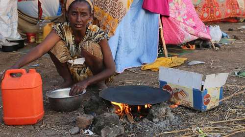 Eine Frau bereitet eine Mahlzeit zu, im Hintergrund sieht man eine provisorische Unterkunft. Foto: WFP