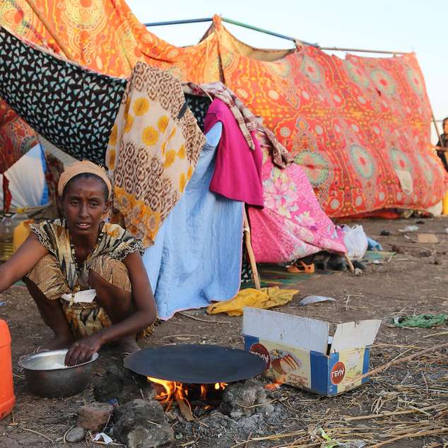 Eine Frau bereitet eine Mahlzeit zu, im Hintergrund sieht man eine provisorische Unterkunft. Foto: WFP