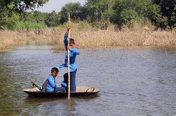 Pakistanische Kinder paddeln mit einem kleinen Boot zur Schule.
