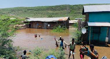 Überschwemmungen in Ostafrika: Überschwemmte Häuser und Menschen, die in Wasser waten.