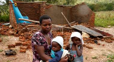 Eine Mutter sitzt mit ihren zwei Kindern vor ihrem zerstörten Haus