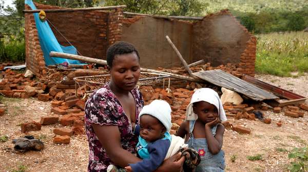Eine Mutter sitzt mit ihren zwei Kindern vor ihrem zerstörten Haus